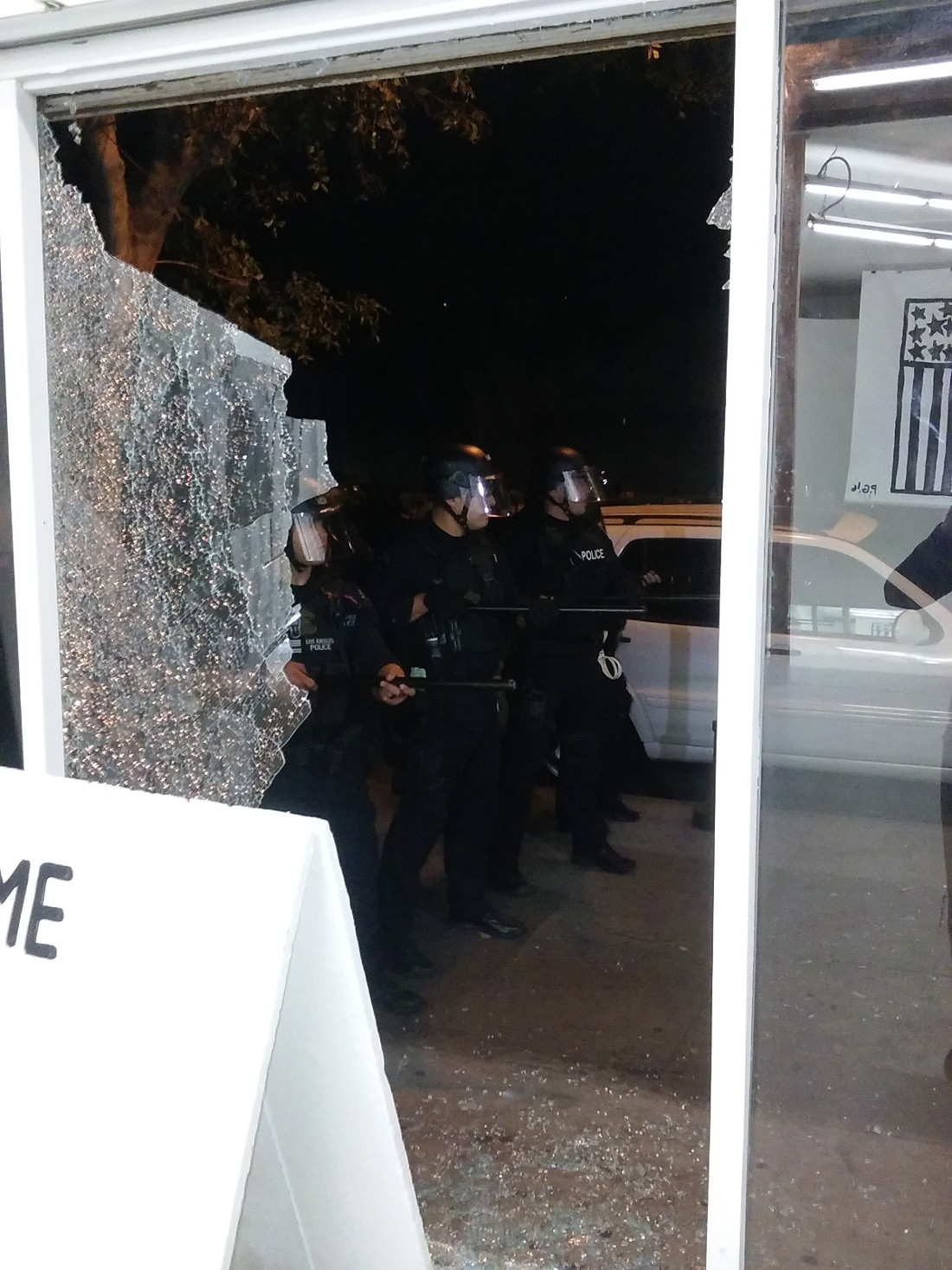 Photograph of police in riot gear kettling anti-Trump protesters through the smashed gallery window