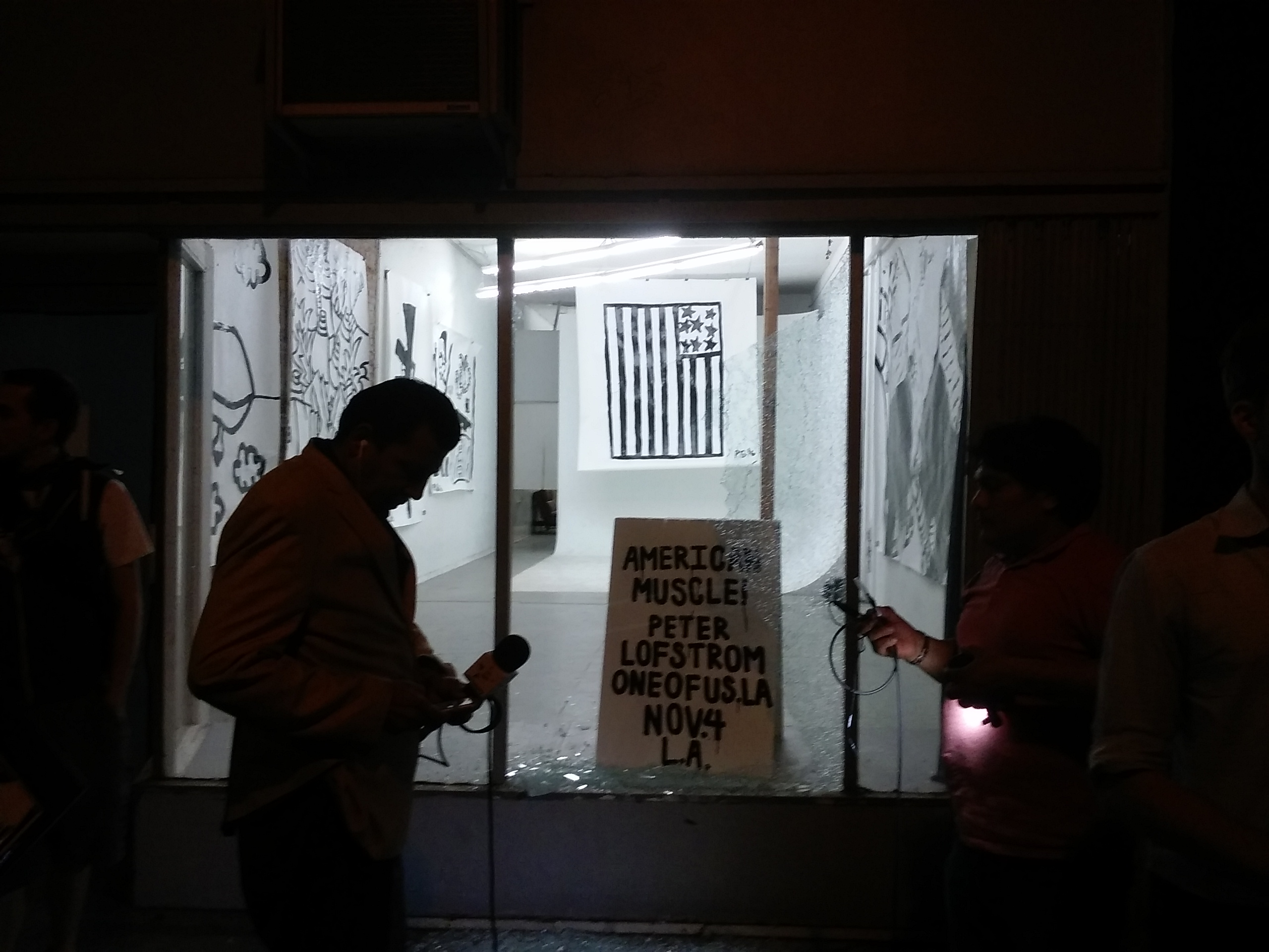 Photograph of television news crew in front of Peter Gustav Löfström's exhibition as seen through smashed gallery window following anti-Trump protests